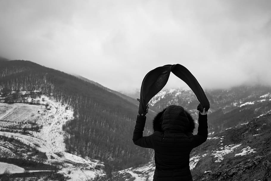 person wearing hooded jacket standing while looking at the snow-covered mountain during daytime, person facing the snow capped mountains HD wallpaper