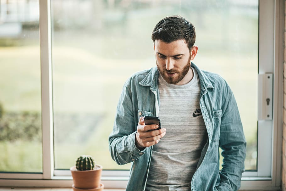 man holding a smartphone near the window, man leaning near window holding phone HD wallpaper