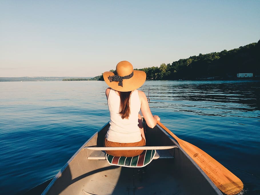 woman wearing sunhat riding boat on body of water, woman in kayak paddling in body of water