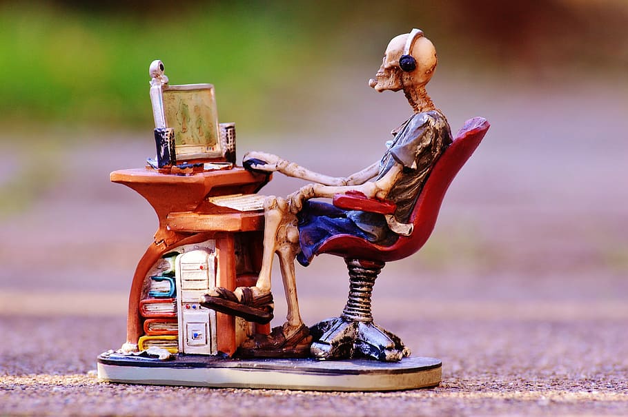skeleton sitting in front of desk ceramic figurine, computer