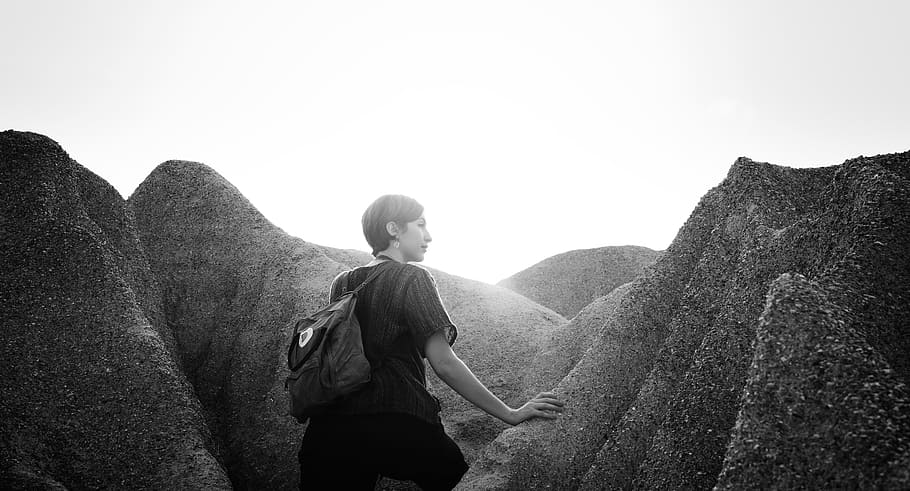 grayscale photo of woman wearing shirt walking in mountains, woman standing surrounded of rocks HD wallpaper