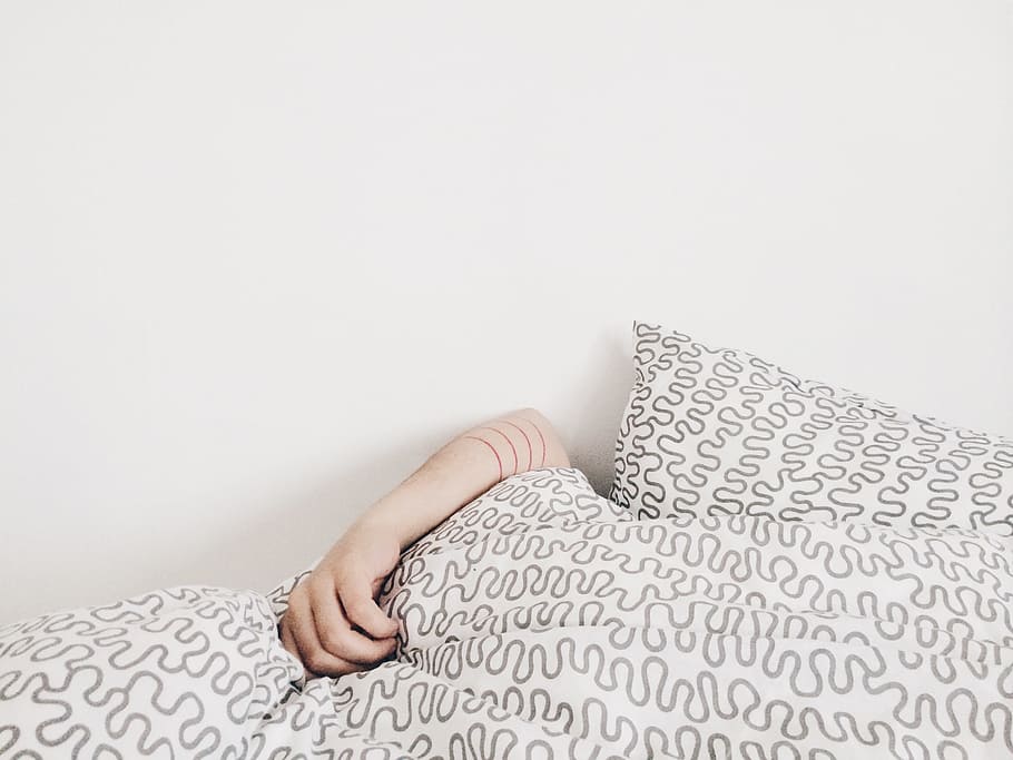 person lying on bed, human hand on grey and white bedspread beside white wall HD wallpaper