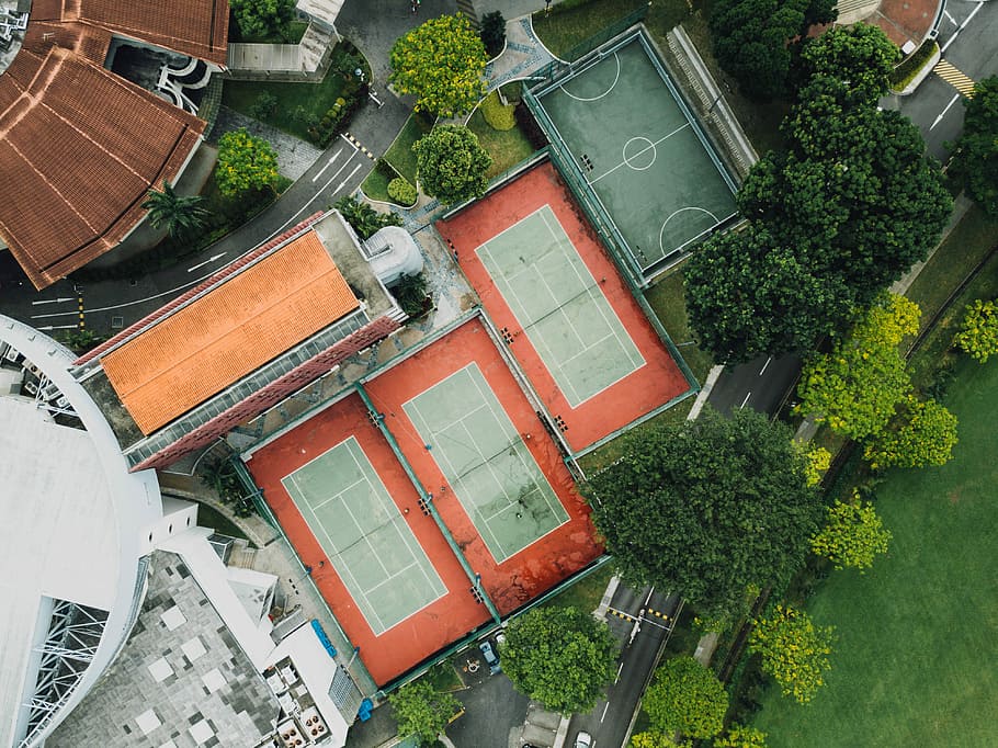 aerial view of basketball and tennis courts, tennis and basketball courts near tall trees and concrete buildings aerial photography