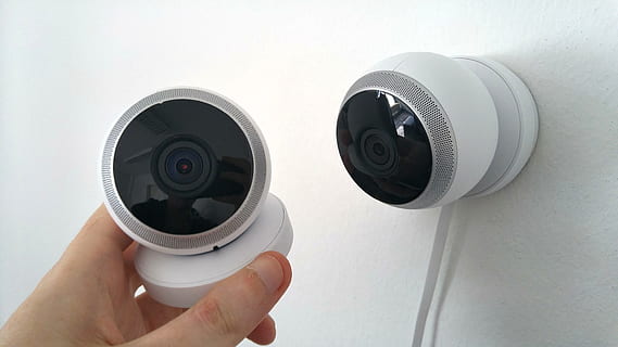 person holding white security camera beside wall-mounted security camera HD wallpaper