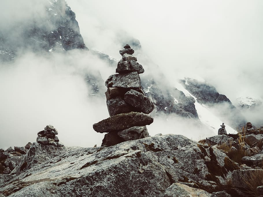 mountain covered in white fog, brown stack stone cairn with steams on cliff