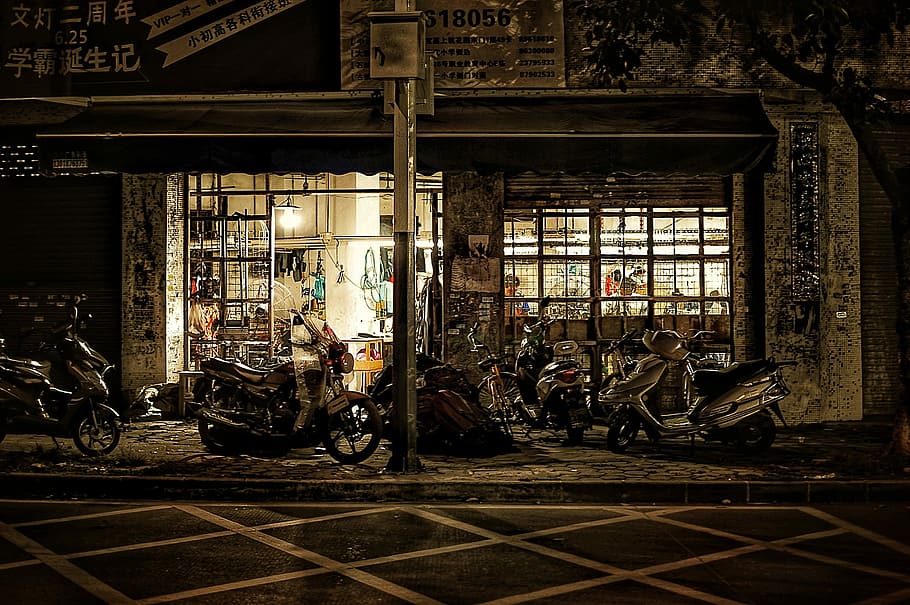 several motorcycles parked on storefront at nighttime, motorcycle in front of store