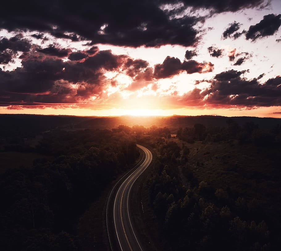 aerial view of a road surrounded by trees during sunset, areal photography of road between trees under golden hour