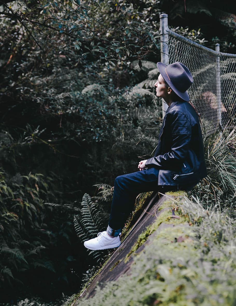person sitting on gray concrete wall, man sitting on rock beside fence HD wallpaper