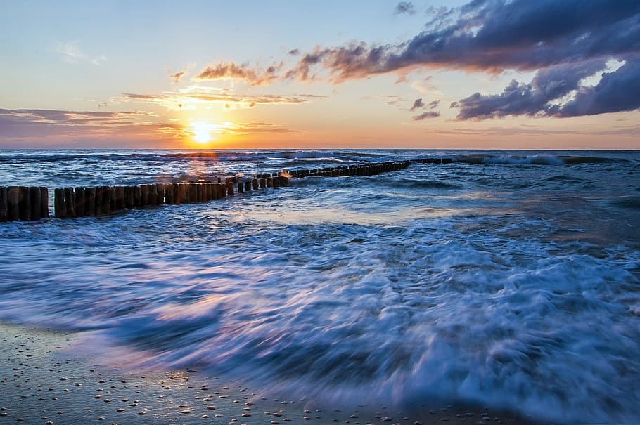 brown wooden docks on blue boy of water at daytime, sea waves crashing on shore during golden hour HD wallpaper