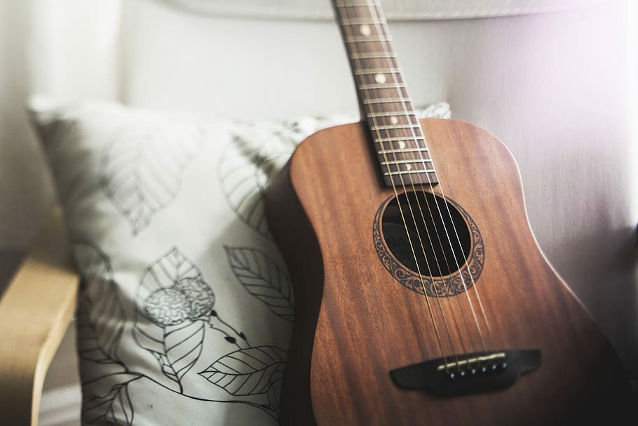selective focus photo of brown guitar on white pillow, brown ukulele and white throw pillow on chair HD wallpaper