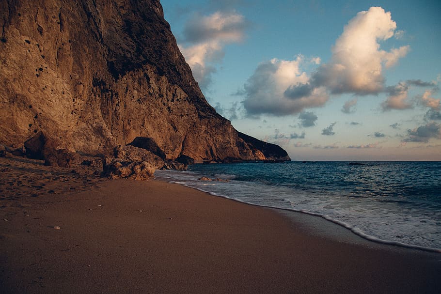 blue ocean water near rock formation, photo of brown mountain near body of water HD wallpaper