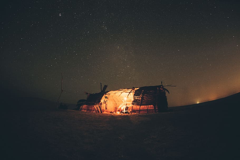 person inside brown house with light during nighttime, man inside the hut with lamp during nighttime HD wallpaper