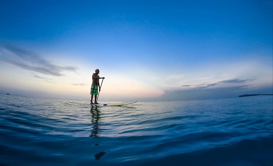 panoramic photography of man riding paddle board on body of water