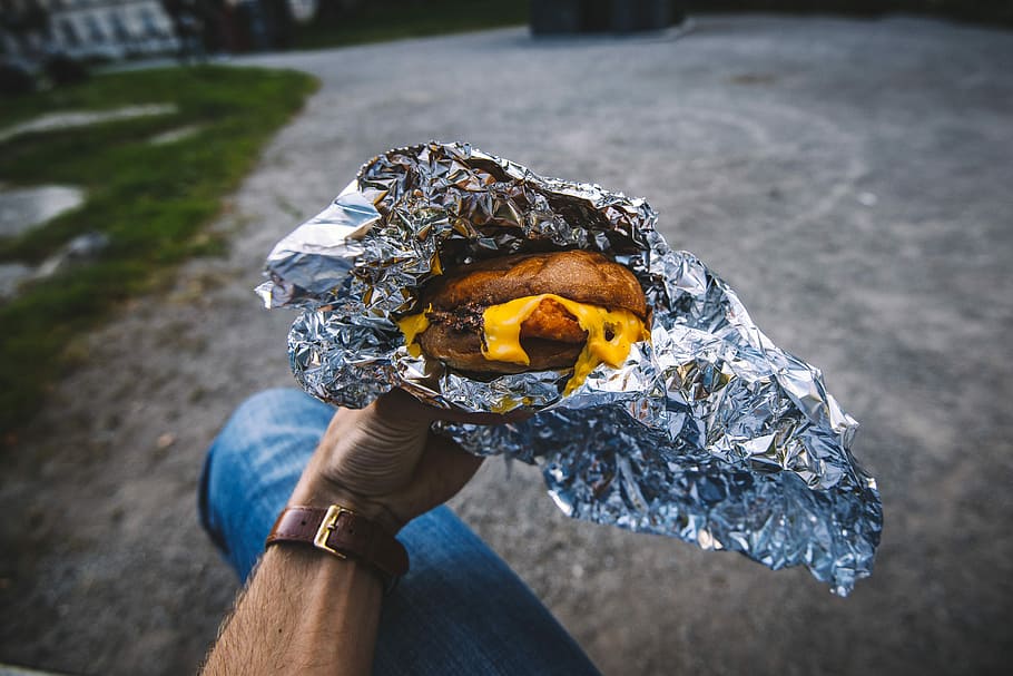 cooked food in foil pack, person holding foil wrapped melted cheese burger