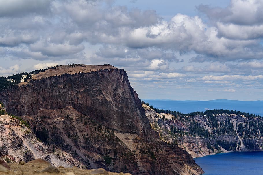 aerial photo of mountain near body of water, gray rock mountain under blue sky beside body of water at daytime HD wallpaper