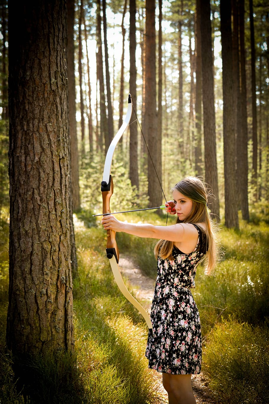 woman in black floral mini dress holding long bow standing beside tree HD wallpaper