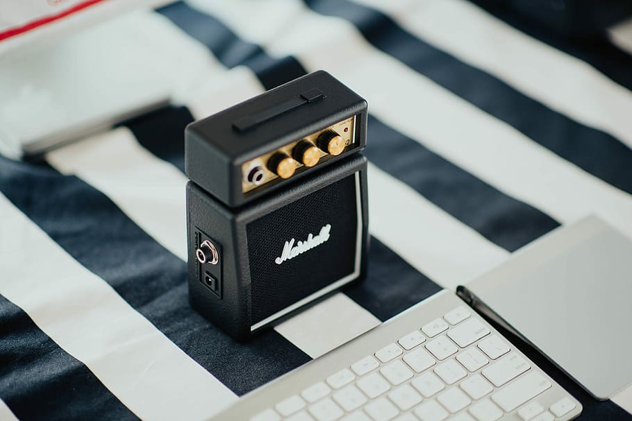 black Marshall portable speaker near white computer keyboard on black and white striped textile, guitar pedal beside apple magic keyboard on white and black striped textile HD wallpaper