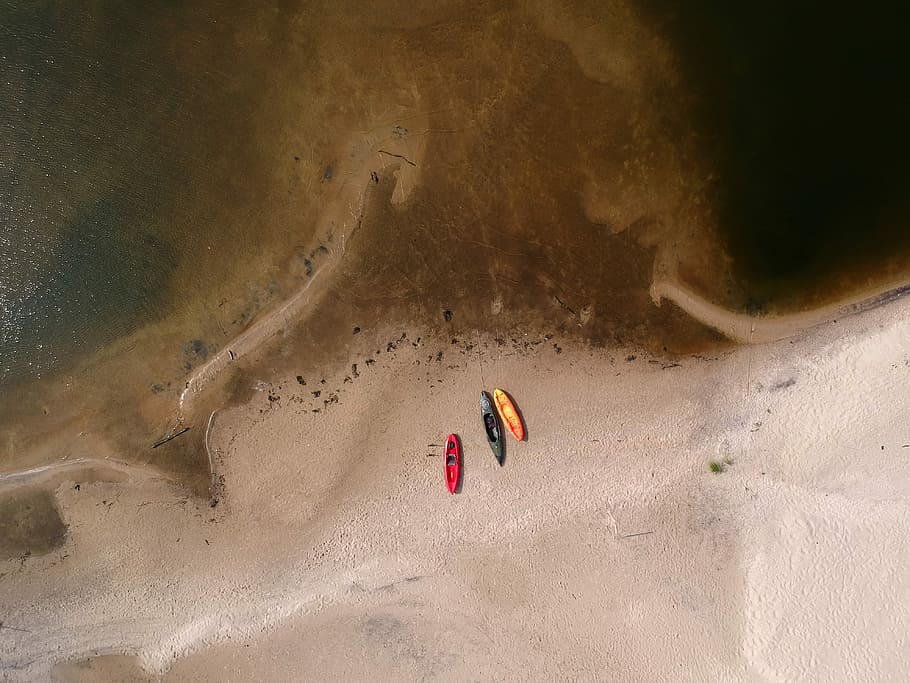 aerial photography of three kayaks near body of water, birds eye view of three assorted-color kayaks on brown sand