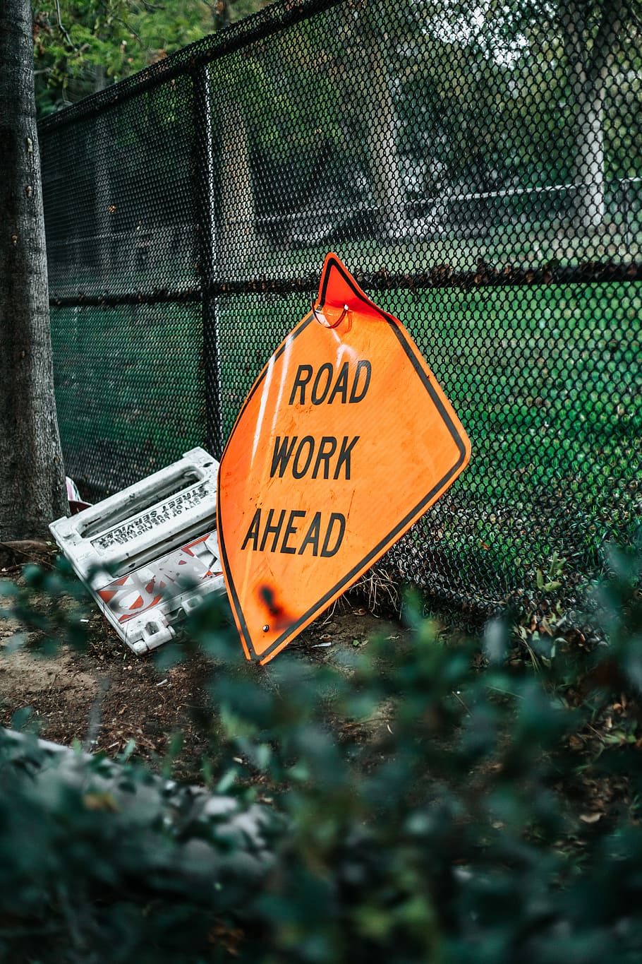 road work ahead signage leaning on chain link fence, road work ahead signage
