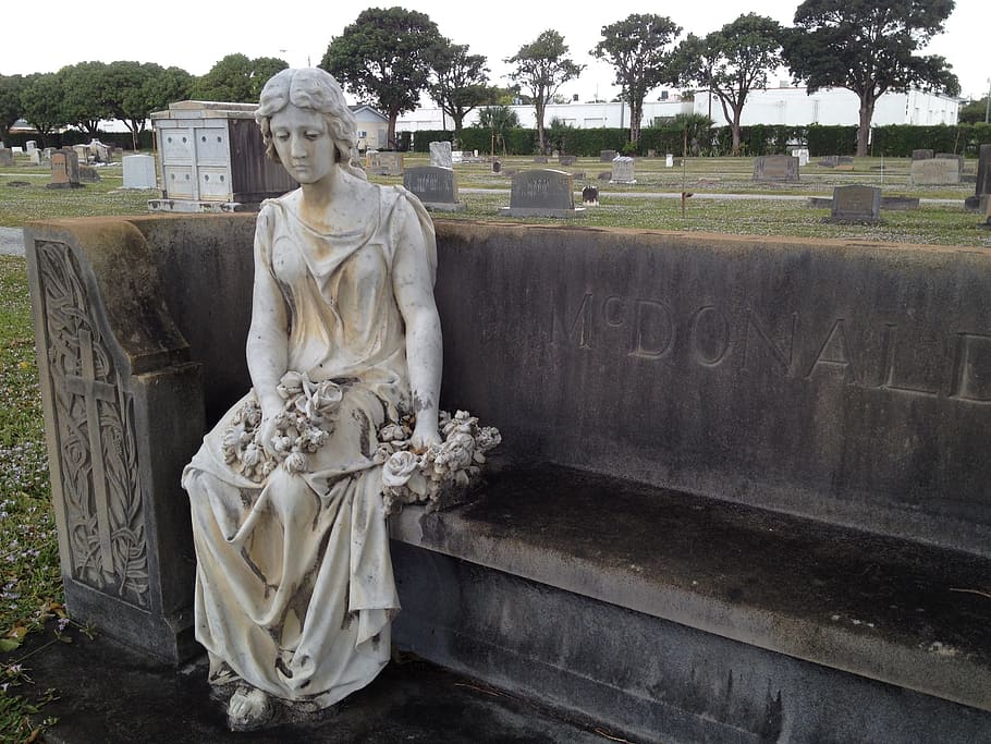 women's concrete statue sitting on black concrete bench, graveyard