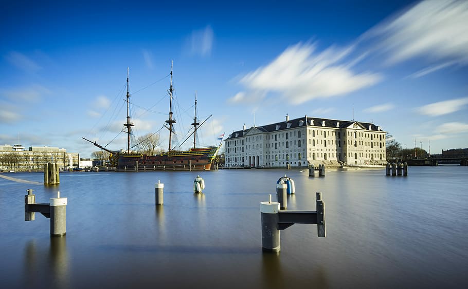 white concrete structure during daytime, brown sailing ship on body of water near white building HD wallpaper