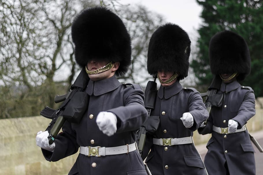 three Queen's guards carrying sub-machine guns, three soldiers marching while holding guns