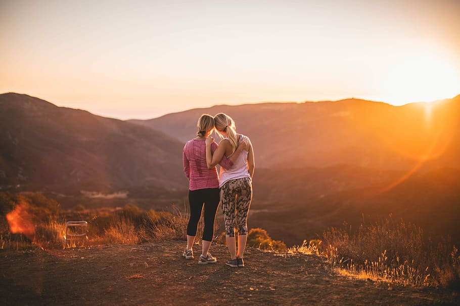 two women standing on moutain, two woman standing on mountain cliff during golden hour HD wallpaper