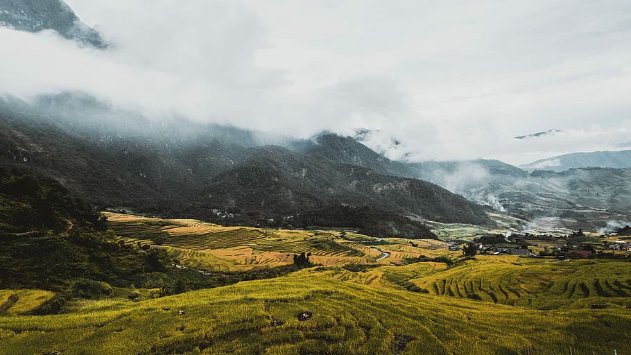 aerial photography of grass field, mountain near the green field under cloudy sky HD wallpaper