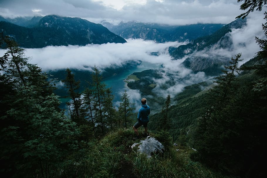 person standing on green cliff under blue sky, man standing on top of mountain under cloudy sky during daytime HD wallpaper