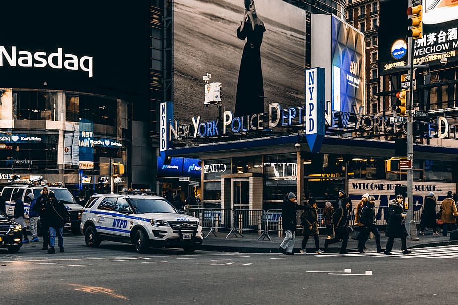 people walking on pedestrian lane near vehicles, people standing near New York Police Dept. building