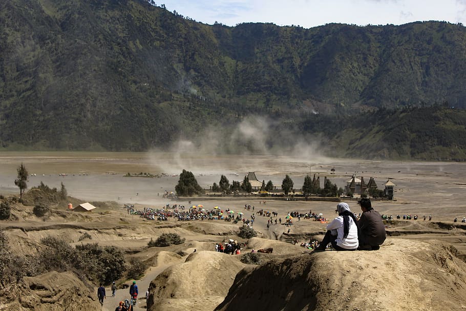 two people sitting on boulder on front of mountain, bromo, horse