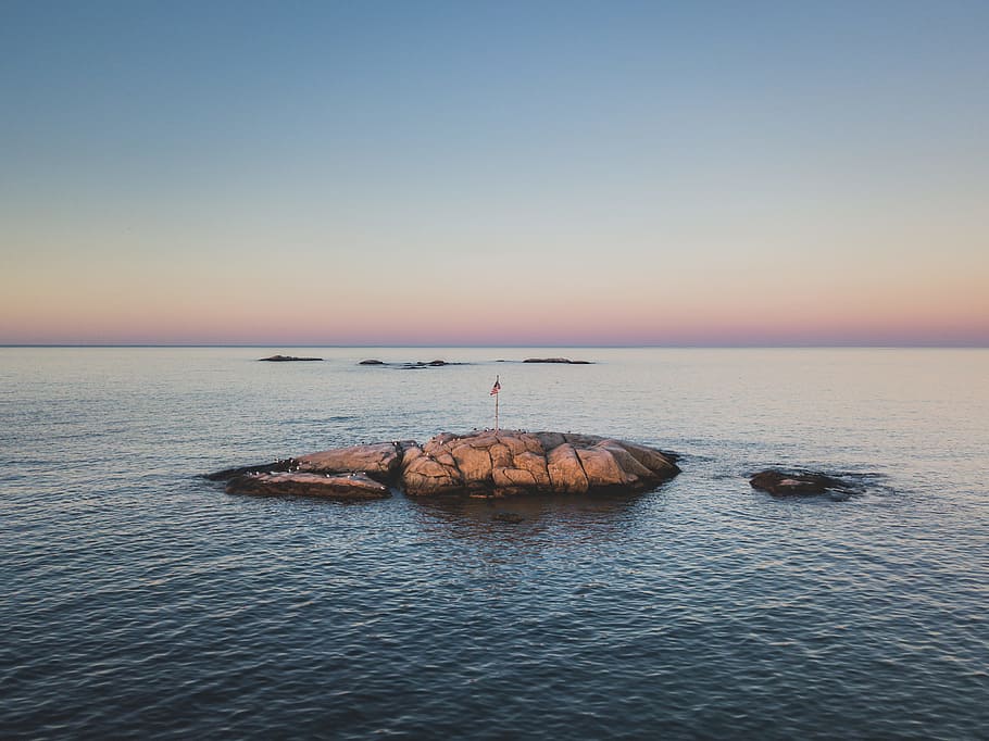 landscape photography of red flag on rock in the middle on ocean, rock formation with flag during sunrise HD wallpaper