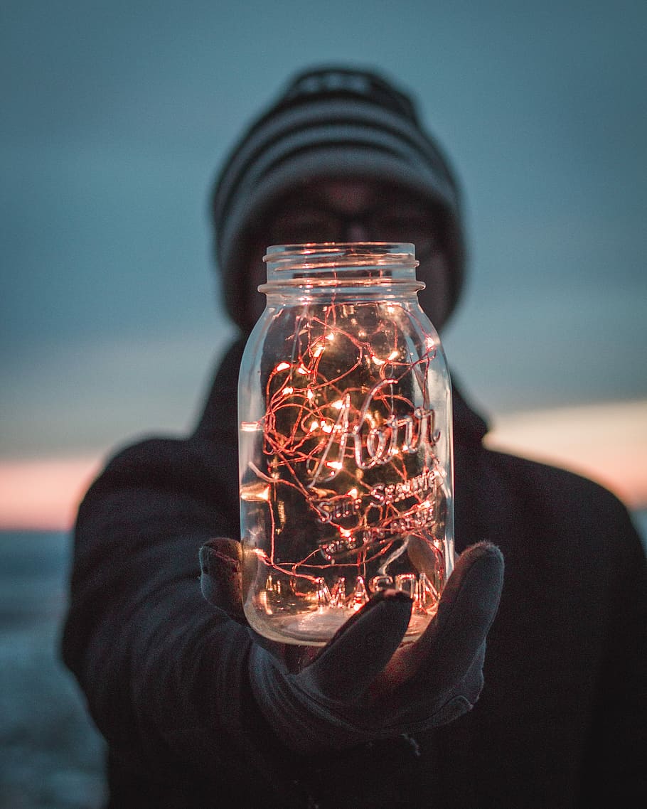 person holding glass mason jar with string lights, person holding a jar with red light strip inside