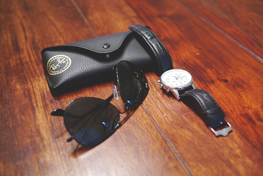 black Ray-Ban Aviators on wooden floor beside round silver-colored watch
