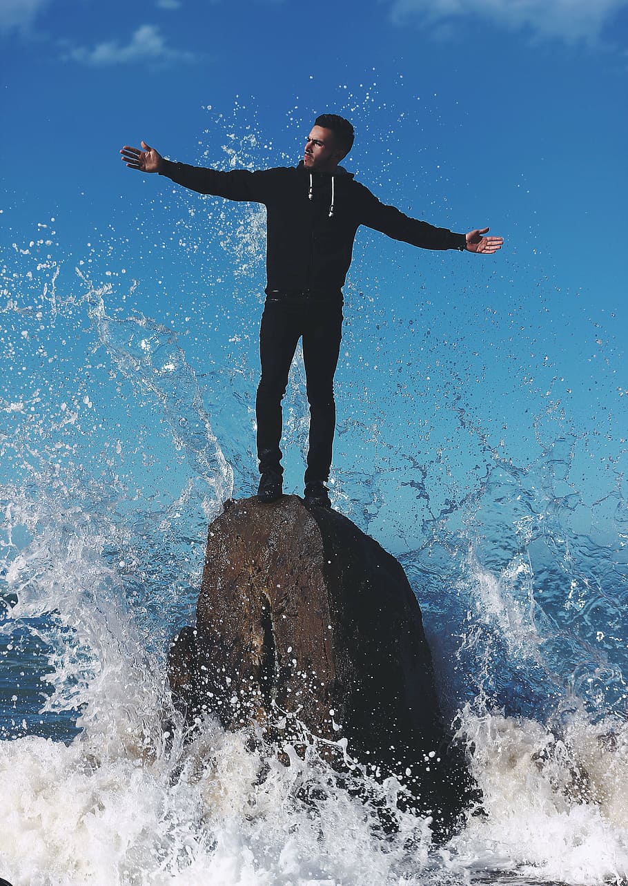 man standing on rock in water, guy, wave, splash, formation HD wallpaper