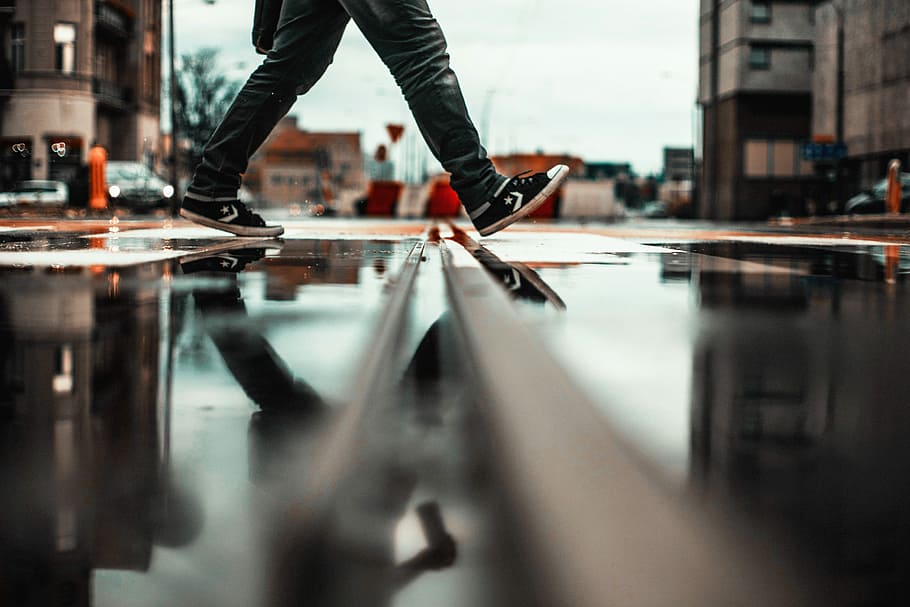 person walking in wet road, low-angle of person walking on wet road