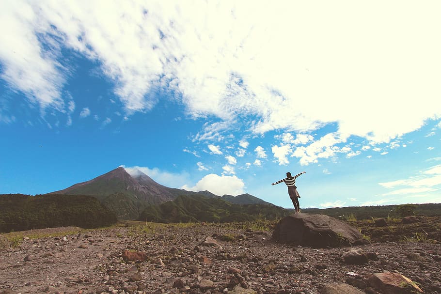 woman standing on rock formation near mountain under blue clouds during daytime HD wallpaper