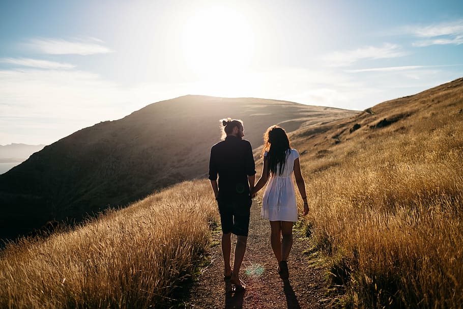couples holding hands while walking on brown mountain at golden hour HD wallpaper