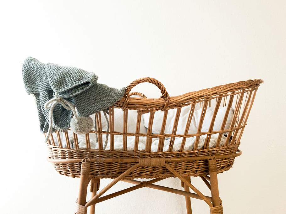 gray textile hanging on brown wicker basket, baby's brown wicker bassinet with gray blanket
