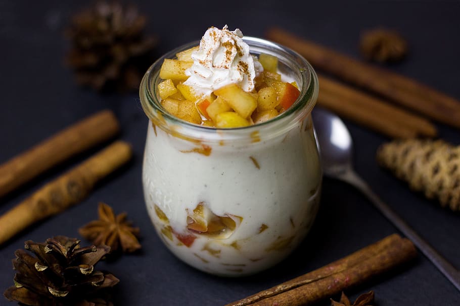 glass with cream and fruit cubes surrounded with cinnamon sticks on the table HD wallpaper