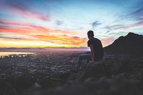 man sitting on hill with cityscape view, valley, cliff, sunset HD wallpaper