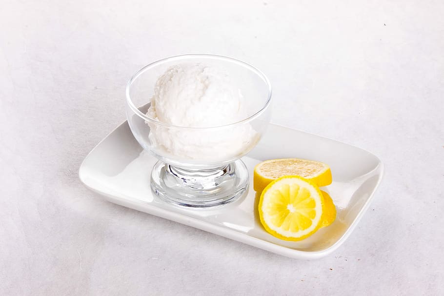 sliced lemon near short-stem glass on white ceramic tray, ice cream