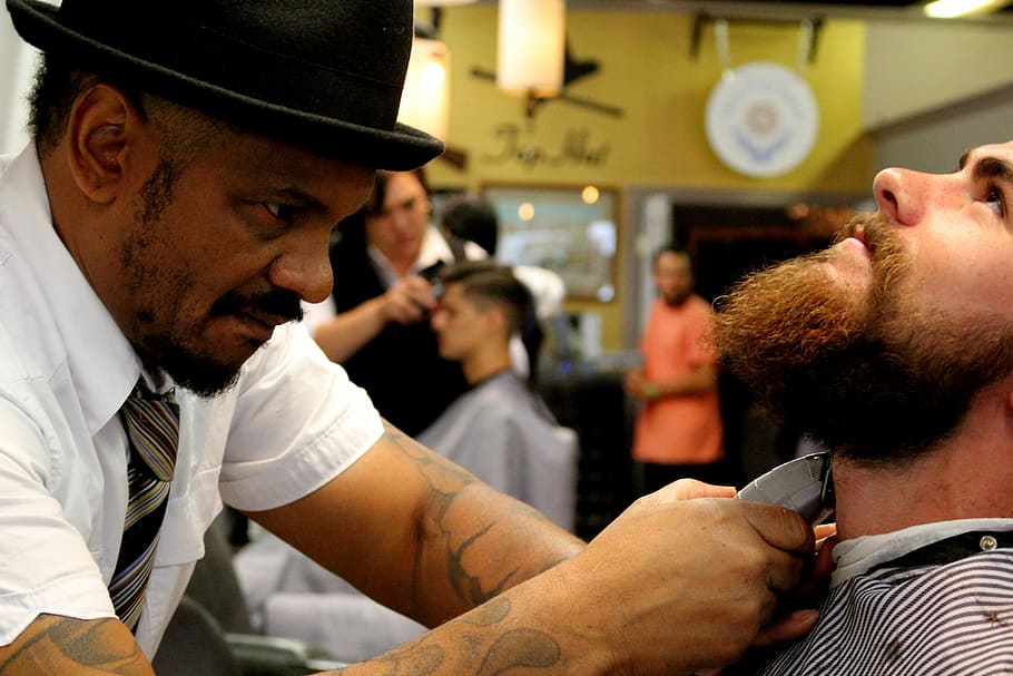 man trimming another man's beard using gray shaver, Barber Shop
