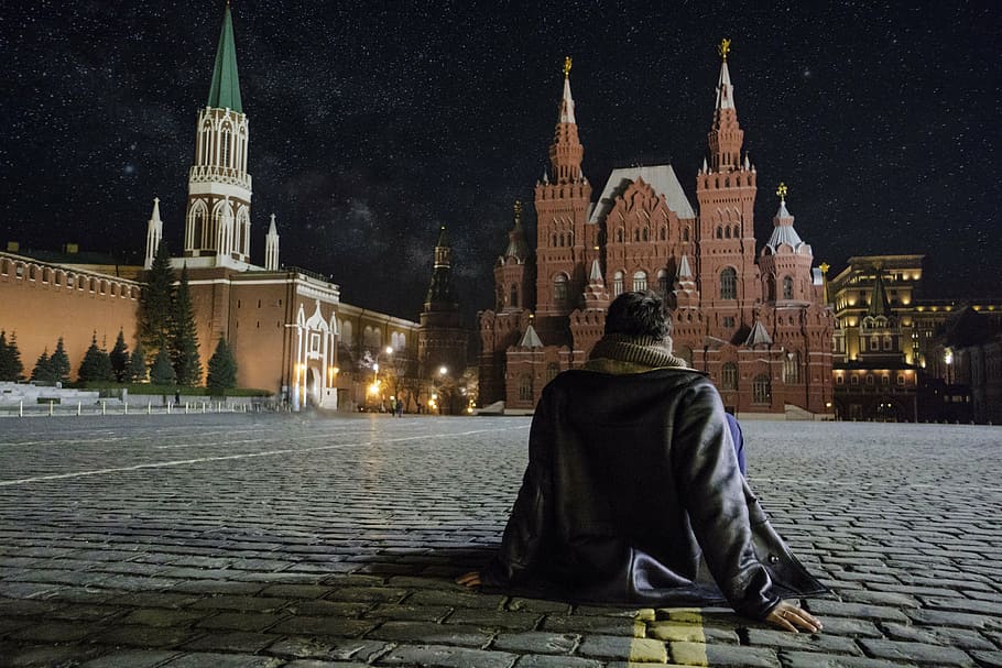 person sitting on street in front of brown brick building, red square HD wallpaper