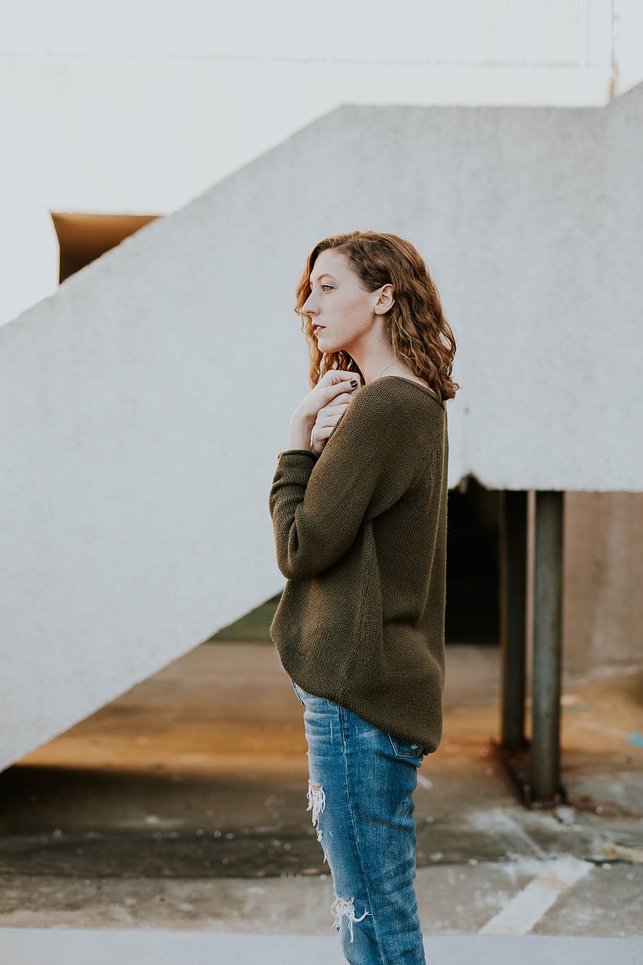 woman wearing brown sweatshirt and whiskered distressed blue jeans, woman standing near white concrete stairway