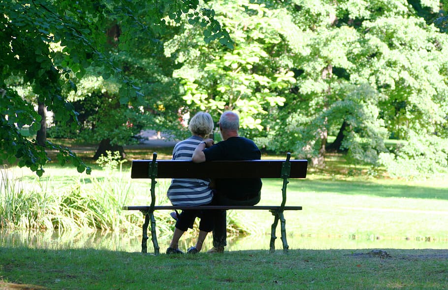 man and woman sitting on the bench surrounded with trees, pair