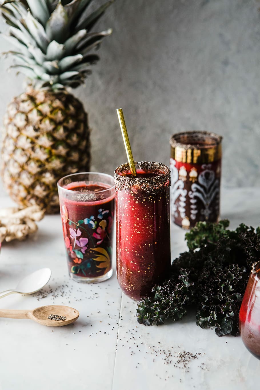 two drinking glass with red liquid near pineapple and green leaves, clear drinking glass near white plastic spoon over pineapple fruit HD wallpaper