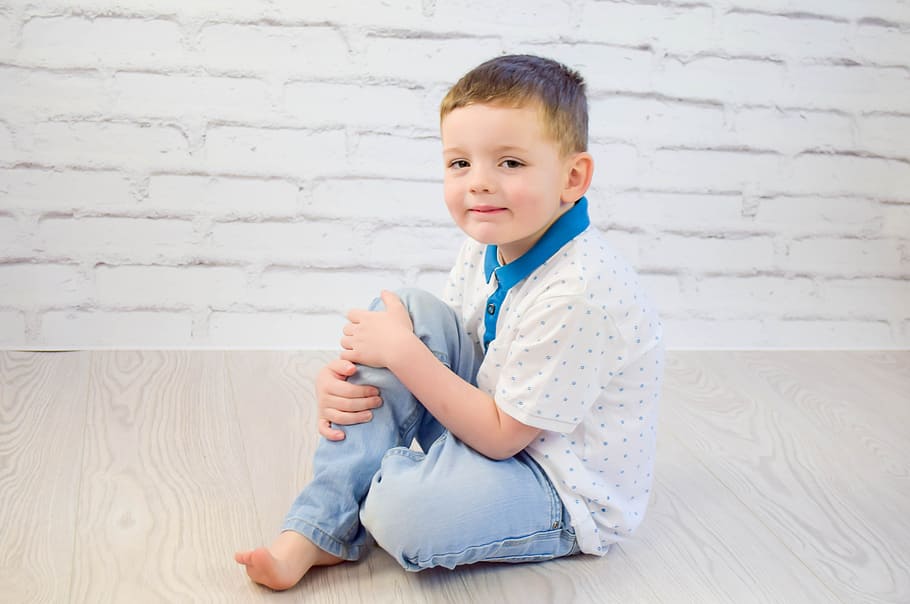 boy in white and blue polka-dots polo shirt and blue jeans sitting on brown wooden floor HD wallpaper