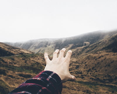 point of view photography of person raising hand towards mountains, person reaching the mountains HD wallpaper