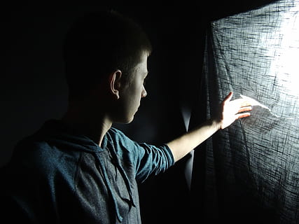 man touching gray textile with light behind, man wearing pullover top peeking inside dark room HD wallpaper